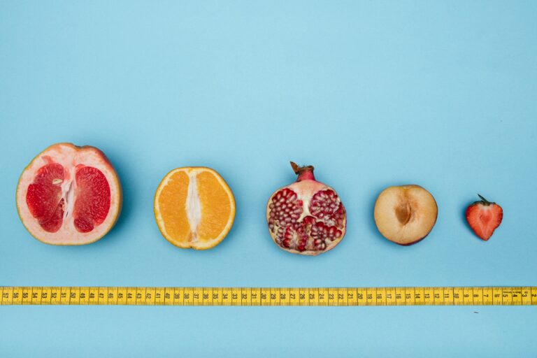 Hilera de frutas abiertas por la mitad, de mayor tamaño a manor, sobre una cinta métrica y con un fondo de color azul celeste