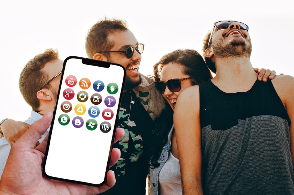 Móvil con iconos de varias redes sociales en primer plano y tres chicos y una chica jóvenes y contentos de fondo